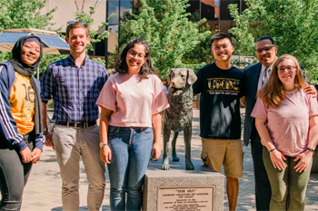 A group of students gathers around a statue of a dog, UMBC's mascot.